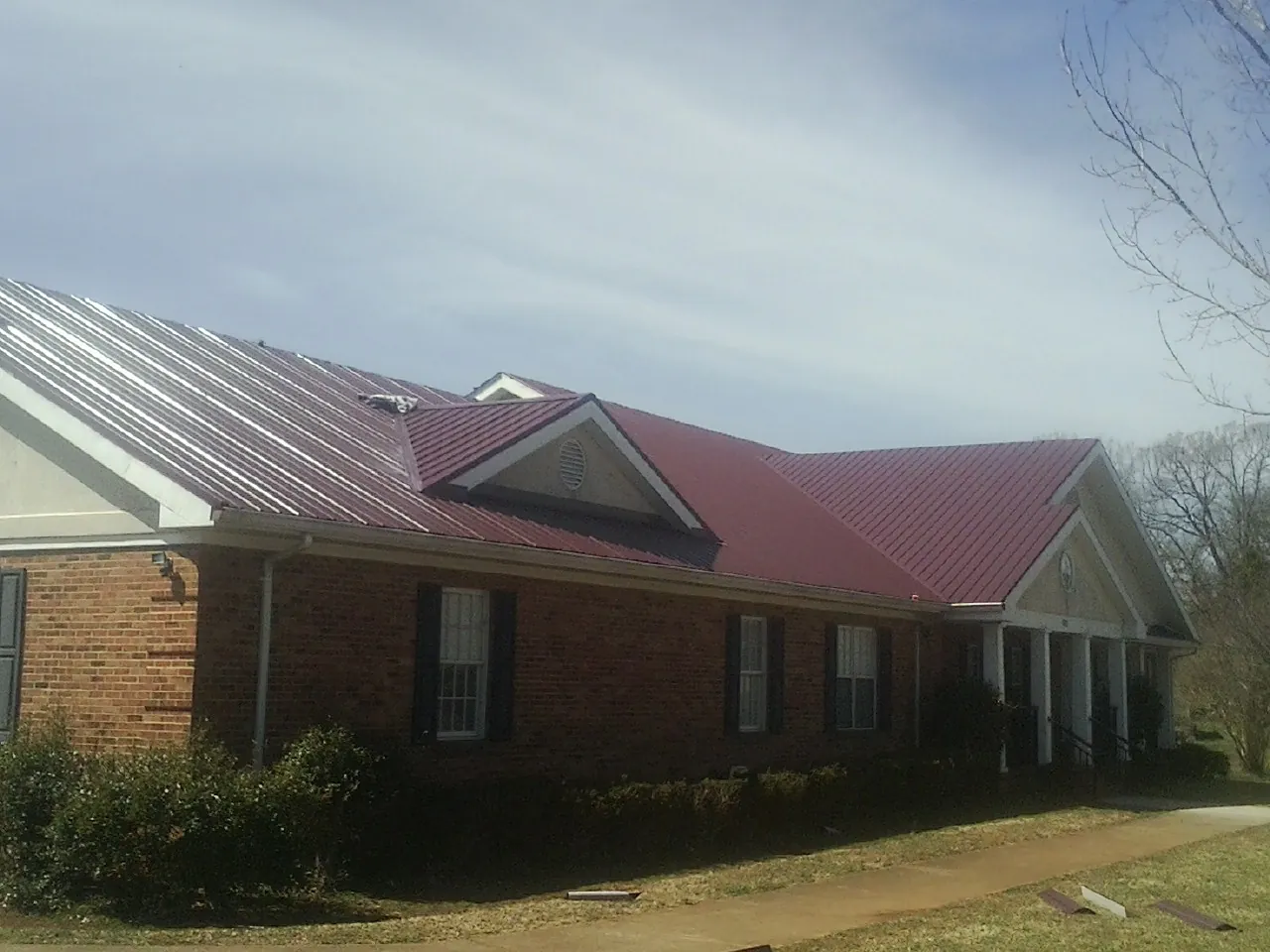 Red metal roof with gabled entries on a long brick building, from a Hail Damage Roof Repair job in Tappahannock