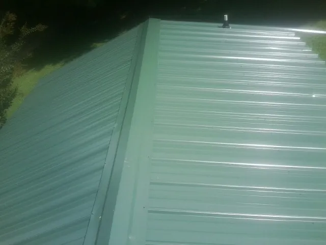 New green metal panels meeting at the ridge of a roof — Flat Roof Repair work by our crew in Tappahannock