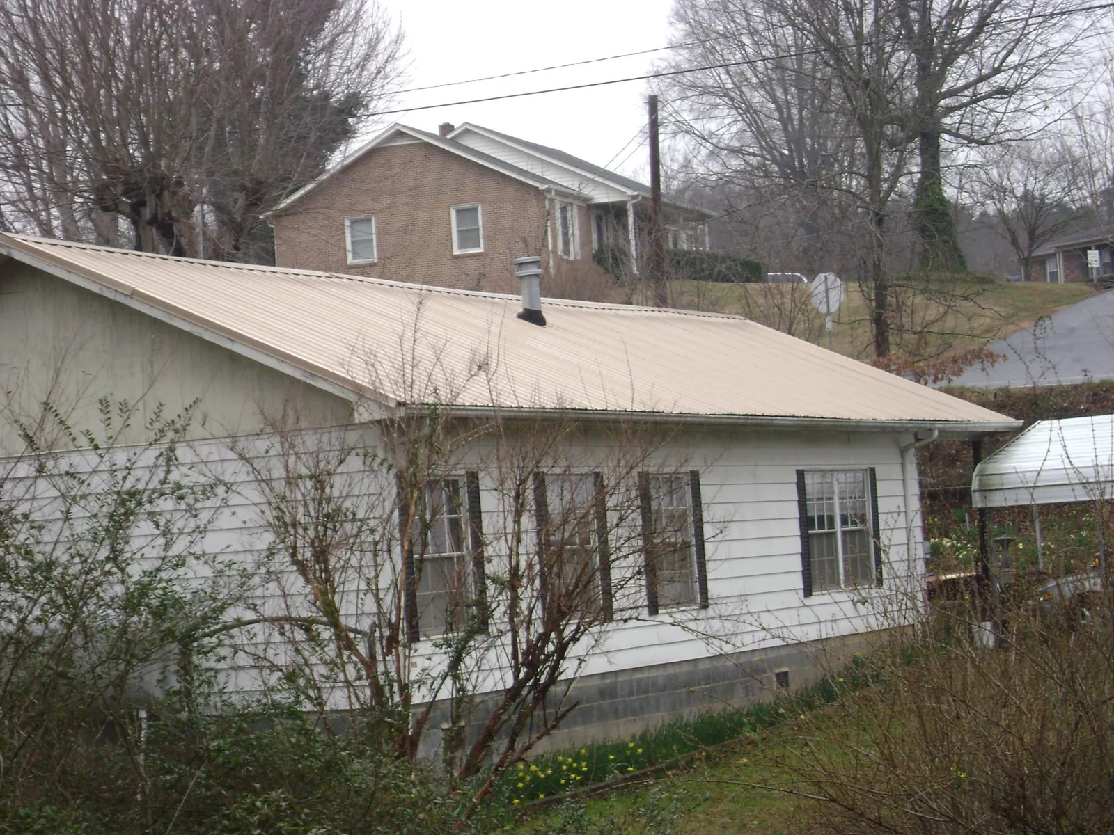 Tan metal roof on a white sided house set into a hillside — Commercial Roofing by Roofing Brothers in Tappahannock